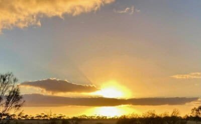 The image is of the sun setting behind a ribbon of clouds
