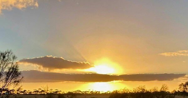 The image is of the sun setting behind a ribbon of clouds