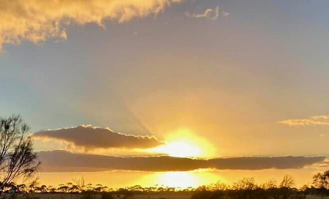 The image is of the sun setting behind a ribbon of clouds
