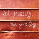 A mahogany wall with white script writing that reads "Feel Yourself, Free Yourself."
