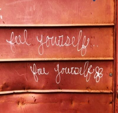 A mahogany wall with white script writing that reads "Feel Yourself, Free Yourself."