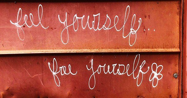 A mahogany wall with white script writing that reads "Feel Yourself, Free Yourself."