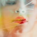 A woman with red lipstick presses her mouth to some cellophane.