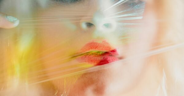 A woman with red lipstick presses her mouth to some cellophane.