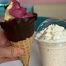 A dipped waffle cone filled with purple and orange swirled ice cream and milk shake topped with a mound of whipped cream