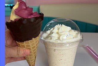 A dipped waffle cone filled with purple and orange swirled ice cream and milk shake topped with a mound of whipped cream