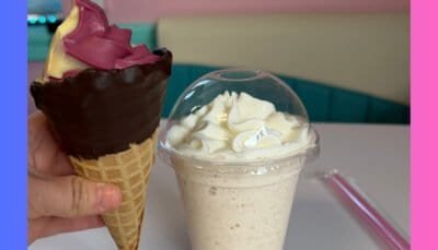 A dipped waffle cone filled with purple and orange swirled ice cream and milk shake topped with a mound of whipped cream