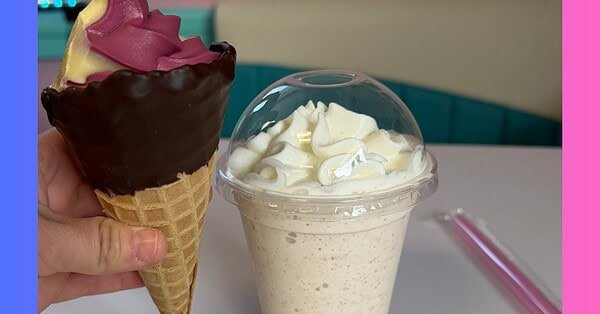 A dipped waffle cone filled with purple and orange swirled ice cream and milk shake topped with a mound of whipped cream