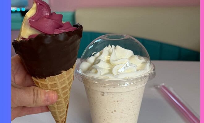 A dipped waffle cone filled with purple and orange swirled ice cream and milk shake topped with a mound of whipped cream