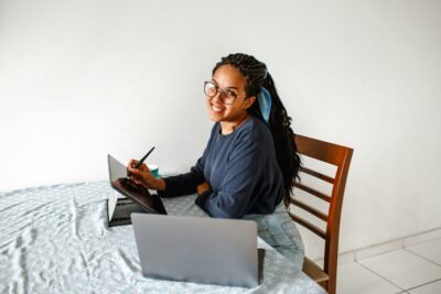 a lady sitting at a table and smiling in from of a laptop and tablet.