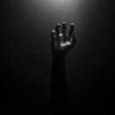 The photo is nearly pitch black, and the faint outline of a hand can be seen reaching upwards towards an unknown light source, as if trying to find hope within the dark