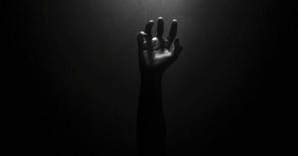 The photo is nearly pitch black, and the faint outline of a hand can be seen reaching upwards towards an unknown light source, as if trying to find hope within the dark