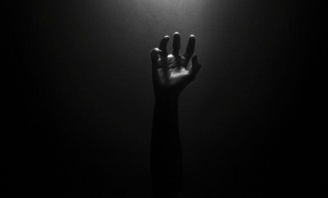 The photo is nearly pitch black, and the faint outline of a hand can be seen reaching upwards towards an unknown light source, as if trying to find hope within the dark