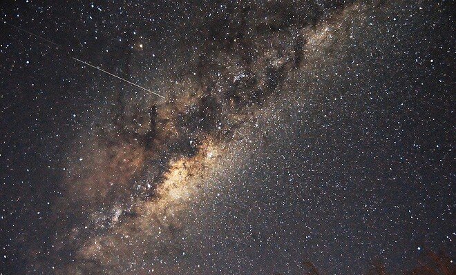 A shooting star streaks across the bright stars outlining the disk of the Milky Way
