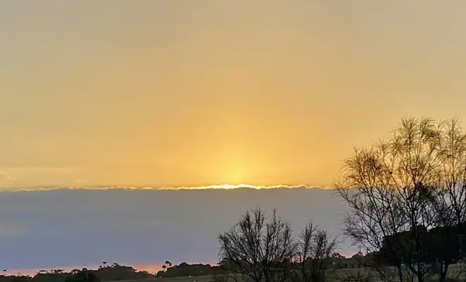 The image is of a fawn twilight sky sitting over the setting sun and a grey cloud band, which could be interpreted as a 'Timeline.'