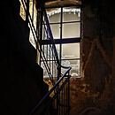 A dark and barely lit staircase with a window facing the fading sun