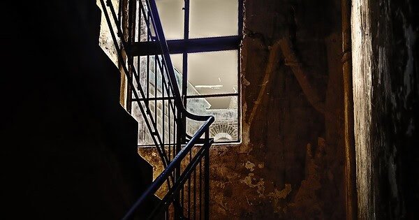 A dark and barely lit staircase with a window facing the fading sun