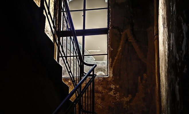 A dark and barely lit staircase with a window facing the fading sun