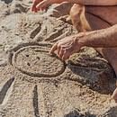 a man draws a sun with a smily face in the sand