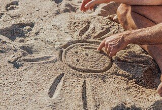 a man draws a sun with a smily face in the sand