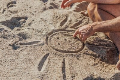 a man draws a sun with a smily face in the sand