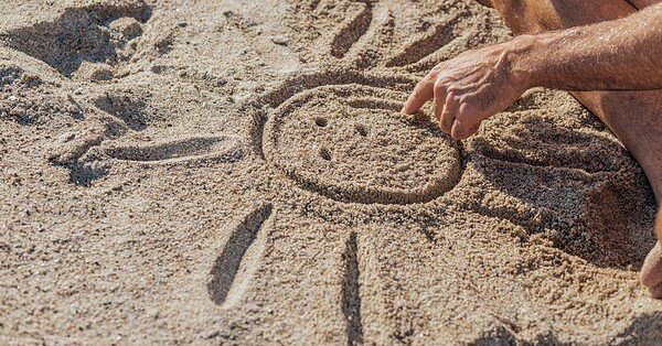 a man draws a sun with a smily face in the sand