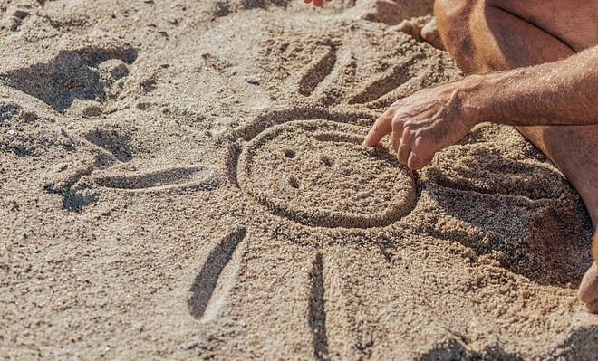 a man draws a sun with a smily face in the sand