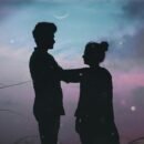 The silhouette of a man and a woman standing outside underneath a twilight sky.