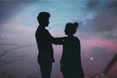 The silhouette of a man and a woman standing outside underneath a twilight sky.