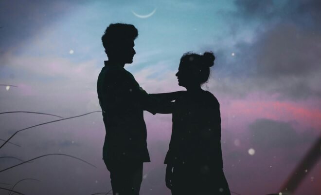 The silhouette of a man and a woman standing outside underneath a twilight sky.