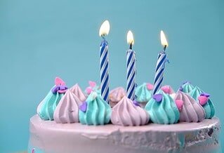 There is a blue background and the top of a pink cake could be seen, covered in blue and pink frosting with three candles on top.
