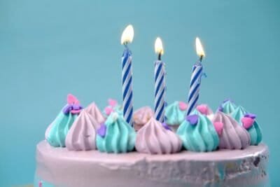 There is a blue background and the top of a pink cake could be seen, covered in blue and pink frosting with three candles on top.