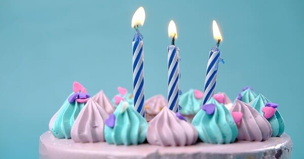 There is a blue background and the top of a pink cake could be seen, covered in blue and pink frosting with three candles on top.
