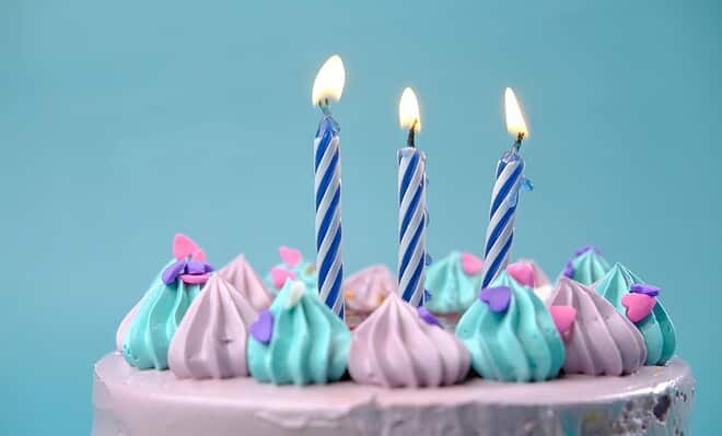 There is a blue background and the top of a pink cake could be seen, covered in blue and pink frosting with three candles on top.