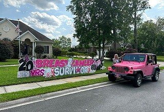 Yard sign says 20 year breast cancer survivor and a pink jeep at the curb