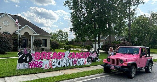 Yard sign says 20 year breast cancer survivor and a pink jeep at the curb