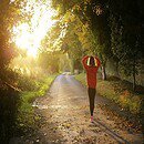 A woman walking in a tree lined forest with a sunlight shining ahead of her.