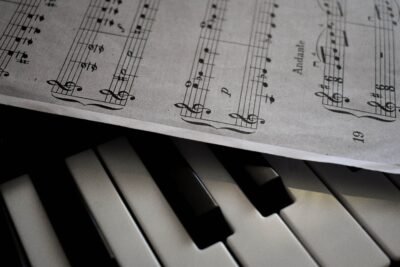 There is a piano shown in the image along with a music sheet that lies slightly atop the piano, faint shadows shown underneath the paper as well.