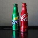 A red Coke bottle and green Sprite bottle sit against a white wall