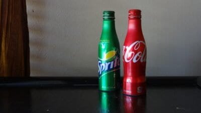 A red Coke bottle and green Sprite bottle sit against a white wall