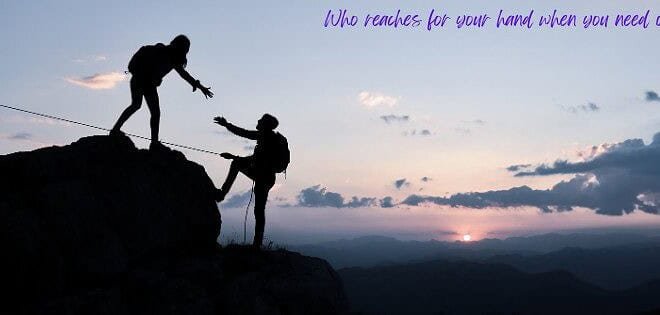Two silhouettes reach the top of a mountain, backed by the soft light of the setting sun