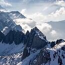 Snow covered mountain peeks along a blue sky horizon with low hanging clouds