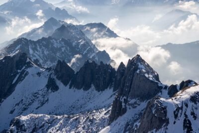 Snow covered mountain peeks along a blue sky horizon with low hanging clouds