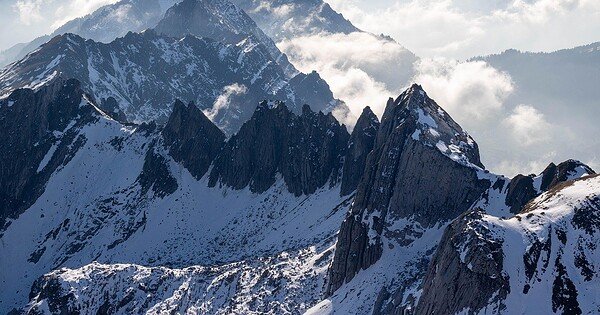 Snow covered mountain peeks along a blue sky horizon with low hanging clouds