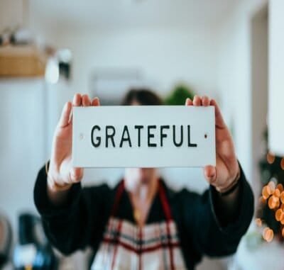 A person holding up a white sign with black lettering that reads gratitude
