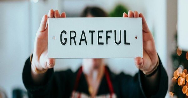 A person holding up a white sign with black lettering that reads gratitude