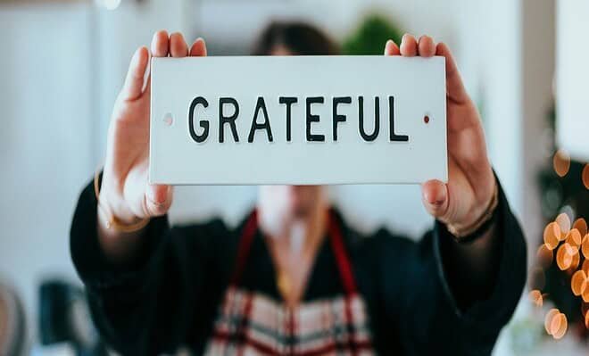 A person holding up a white sign with black lettering that reads gratitude