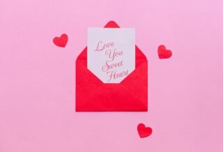 A pink background is set with small red hearts around a small envelope that is opened with a note peaking out that reads "Love you sweet heart"