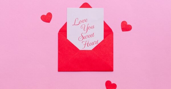 A pink background is set with small red hearts around a small envelope that is opened with a note peaking out that reads "Love you sweet heart"