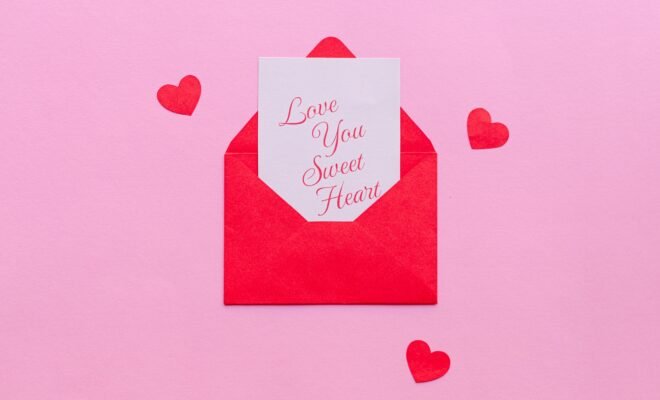 A pink background is set with small red hearts around a small envelope that is opened with a note peaking out that reads "Love you sweet heart"